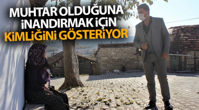 Muhtar olduğuna inandırmak için kimliğini gösteriyor